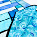 A close-up of a blue and turquoise patterned fabric item, likely a quilt or textile panel, with swirling wave-like motifs and black stitched borders, shown against a white background.
