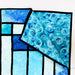 A close-up of a quilted textile featuring geometric panels and a swirled pattern in shades of blue, aqua, and white, separated by black quilting lines.