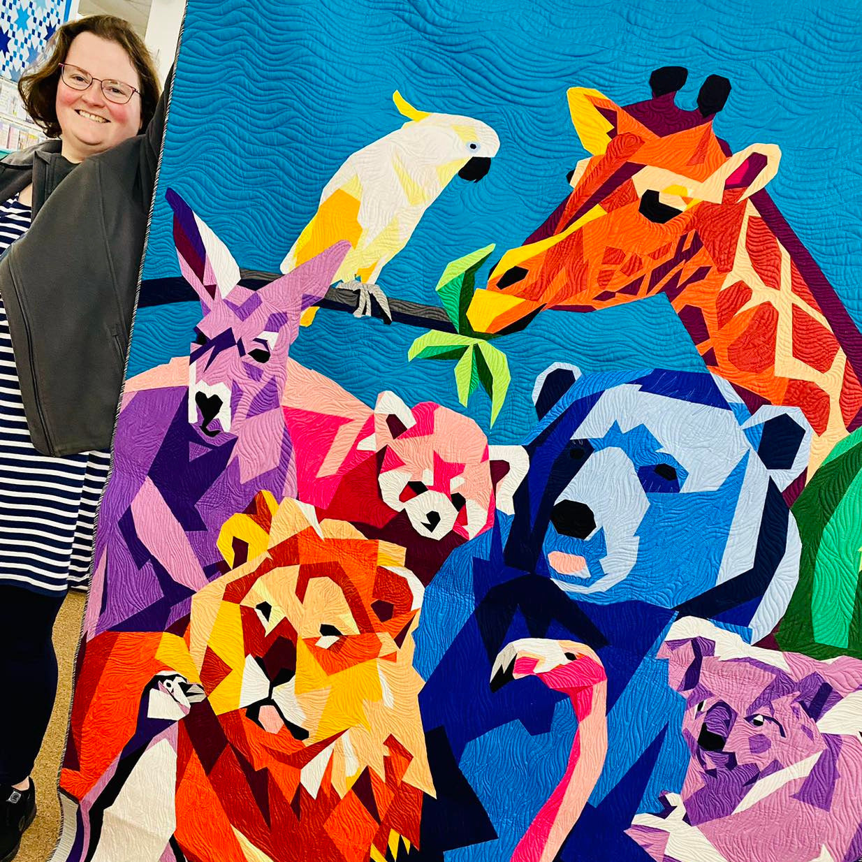 Person standing next to a colorful quilt featuring stylized animals.