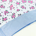 A folded piece of fabric with a white background printed with pink floral clusters and black leaves, layered over a folded piece of light blue and white gingham fabric.
