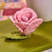 Pink knitted flower on a green base with a white cup in the background