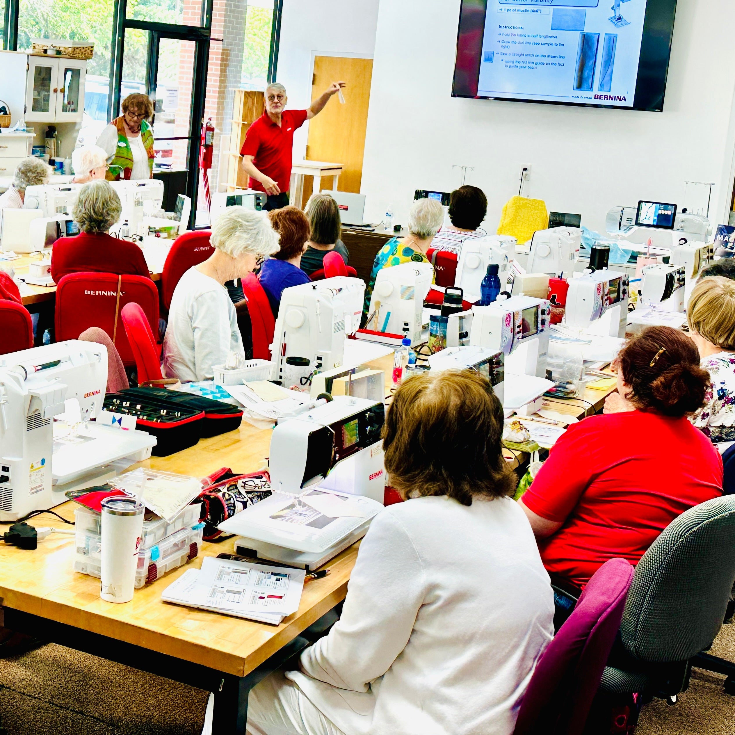 Group of people working on sewing machines in a classroom setting.