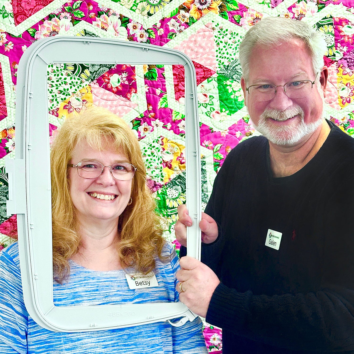 Two people holding a mirror with a colorful quilt in the background