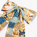 A large fabric bow with a patchwork print featuring blue gingham, brown gingham, floral motifs, and a central gold-toned embellishment, photographed on a white background.