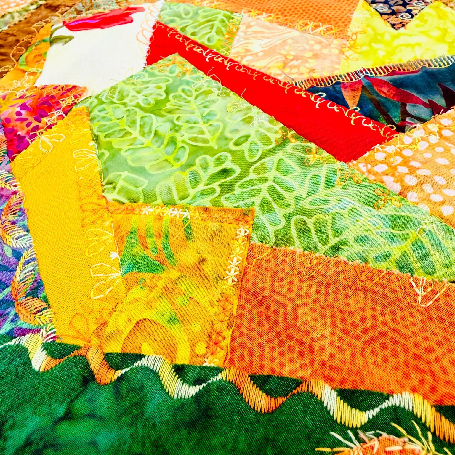 A close-up of a colorful patchwork quilt with various fabric panels in green, orange, yellow, red, and white, featuring different patterns and textures.