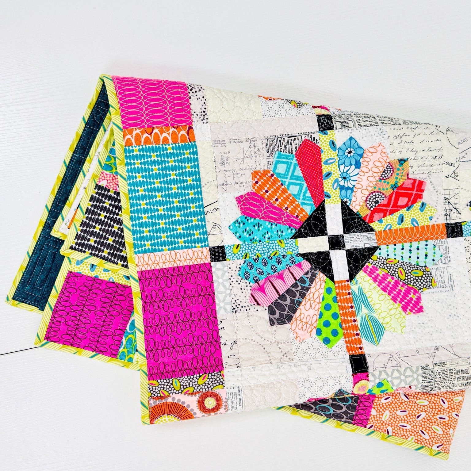 A folded patchwork quilt with a colorful geometric and floral pattern, displayed on a clean white surface.