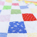 A close-up of a colorful patchwork quilt with various fabric squares in blue, red, green, pink, yellow, and white, stitched together in a grid pattern.