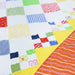 A close-up of a colorful patchwork quilt with white fabric squares, patterned patchwork blocks, and a bright orange quilted section with white wavy lines.