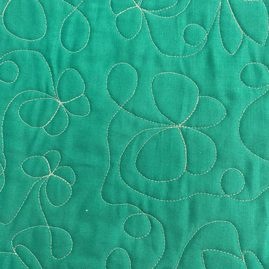 A close-up of a green quilted fabric featuring stitched floral and abstract leaf patterns in a contrasting light beige or cream thread.