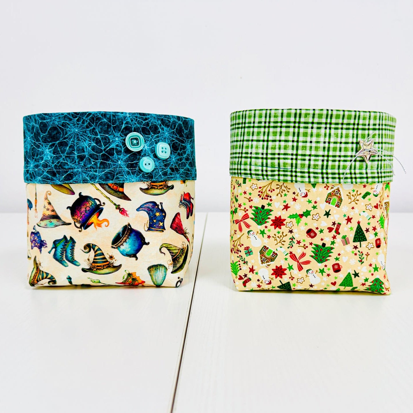 Two small fabric storage boxes or pouches standing upright on a white surface against a white background. The left box has a teal blue top with two buttons and a multicolor fish print body.