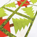 A close-up of a quilted fabric table runner featuring a geometric Christmas tree pattern in green, white, and red, with a decorative olive green patterned border.
