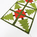 A close-up of a quilted table runner featuring a repeating pattern of green Christmas trees on cream squares, separated by dark green borders and accented with red triangles.