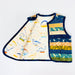 A handmade fabric bib or apron-style pouch laid flat on a white background, featuring a cream-colored front panel with dinosaur illustrations, a navy blue trim, and a side pocket with stacked patterned fabric panels in blue, yellow, green, and orange.
