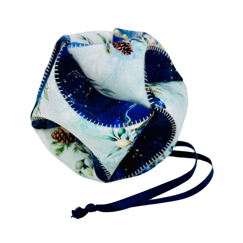 A fabric drawstring pouch with a light blue and navy blue winter forest print, featuring pinecones and white flowers, with a navy blue drawstring cord.