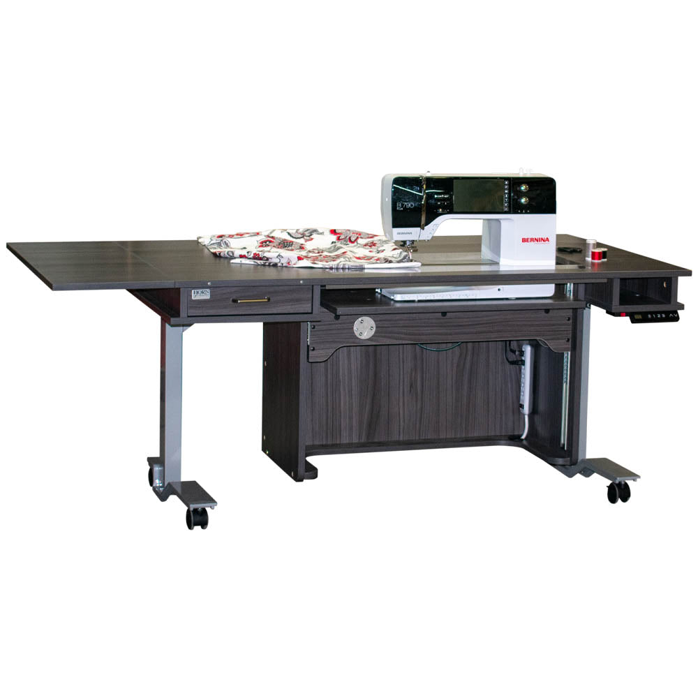 A white, height adjustable sewing table with an electric lift and a filler panel, equipped with wheels for mobility.