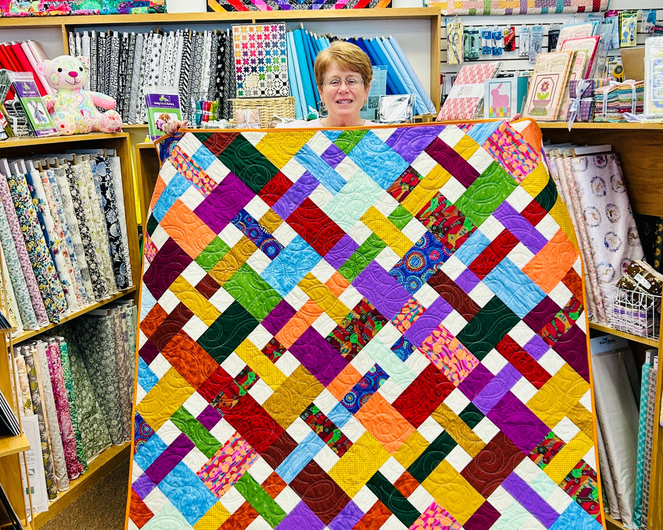 Woman standing behind a colorful quilt in a fabric store.