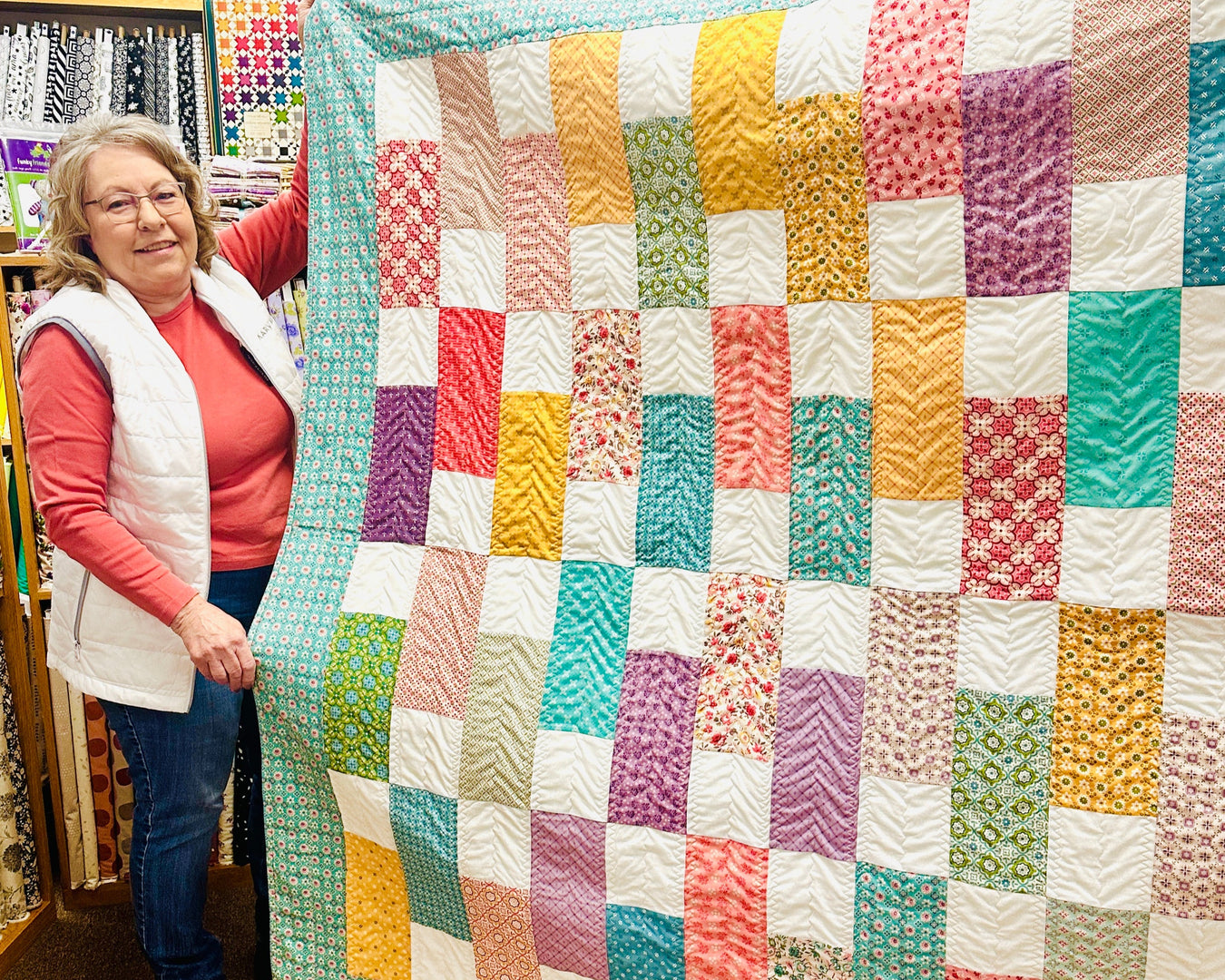 Woman holding a colorful patchwork quilt in a fabric store.