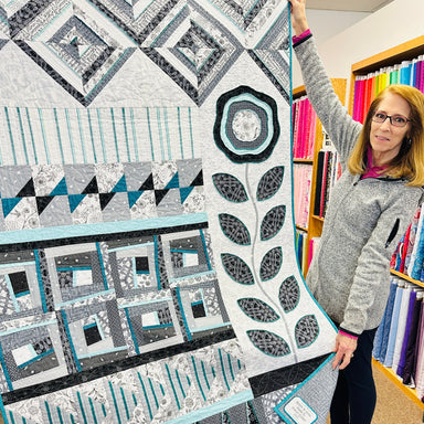 Woman holding a Bloom & Grow quilt with geometric patterns in a fabric store.