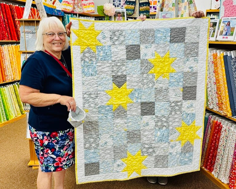 Woman holding a star-patterned quilt in a fabric store