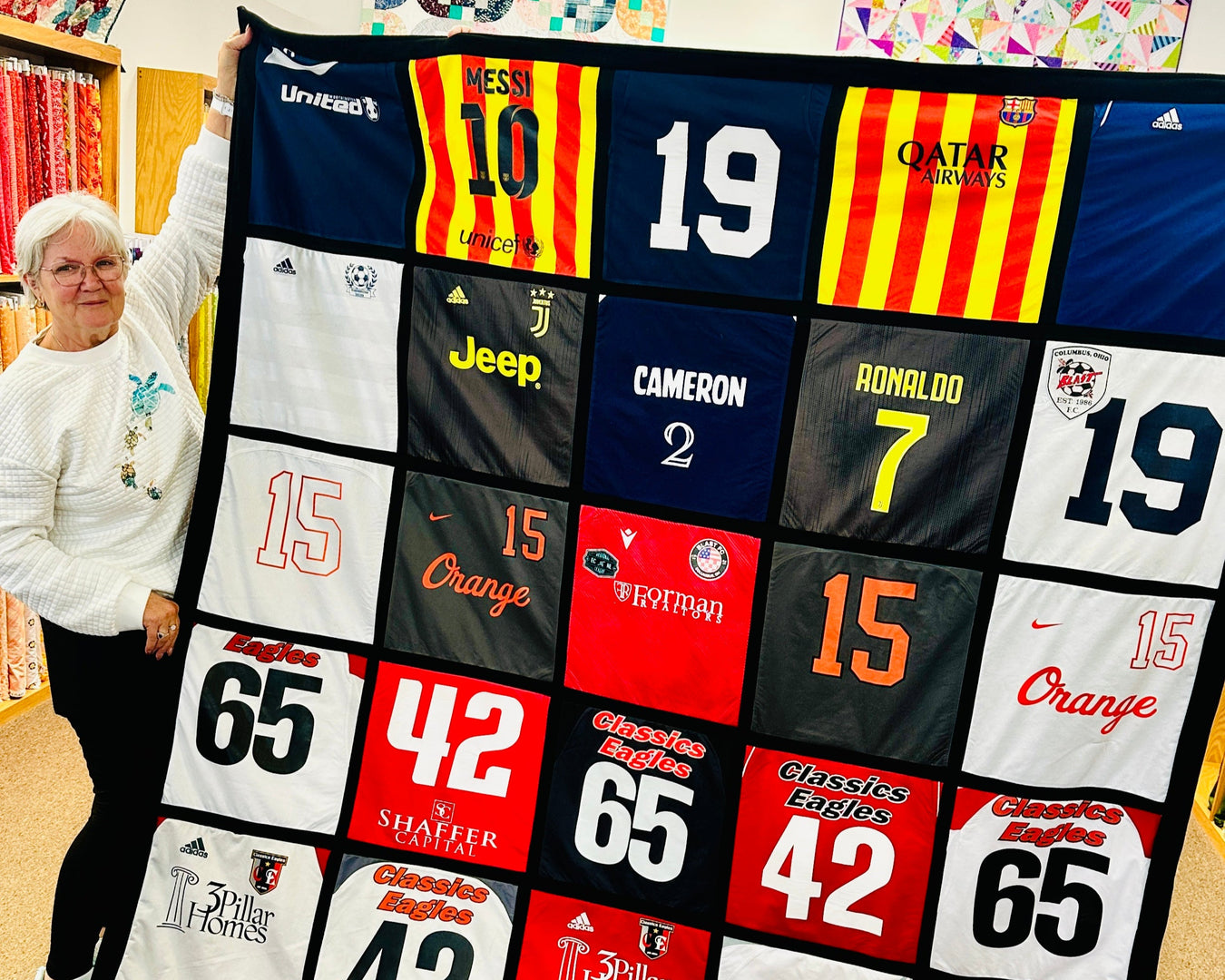 Person holding a quilt with various sports team logos and numbers
