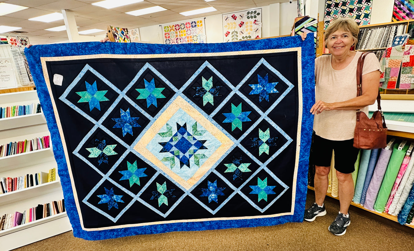 Woman holding a large blue and white quilt in a store setting