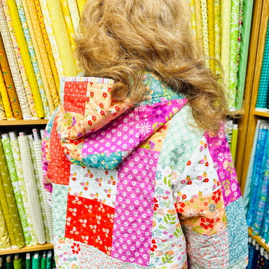 Person wearing a colorful quilted jacket in a fabric store