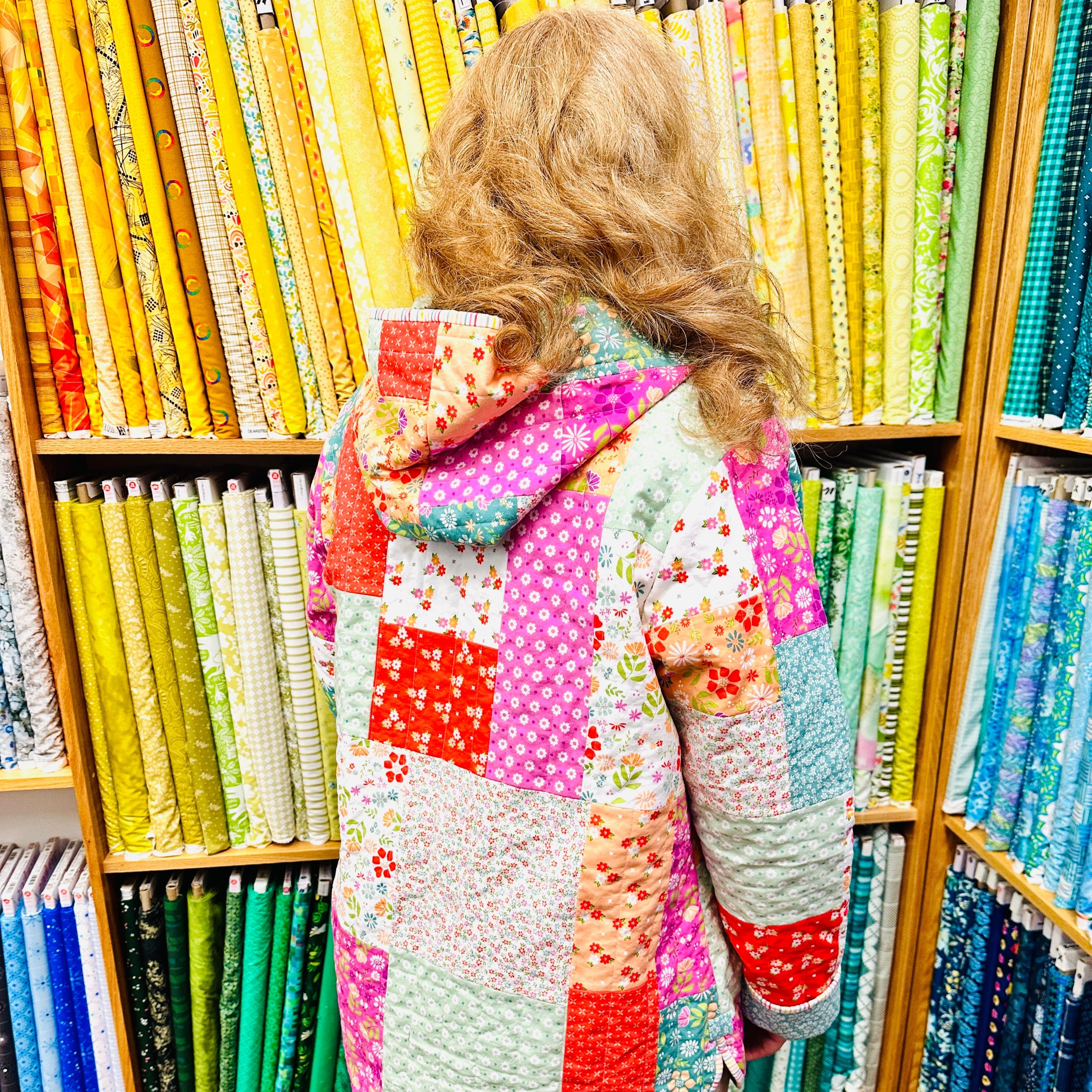 Person wearing a colorful quilted jacket in a fabric store