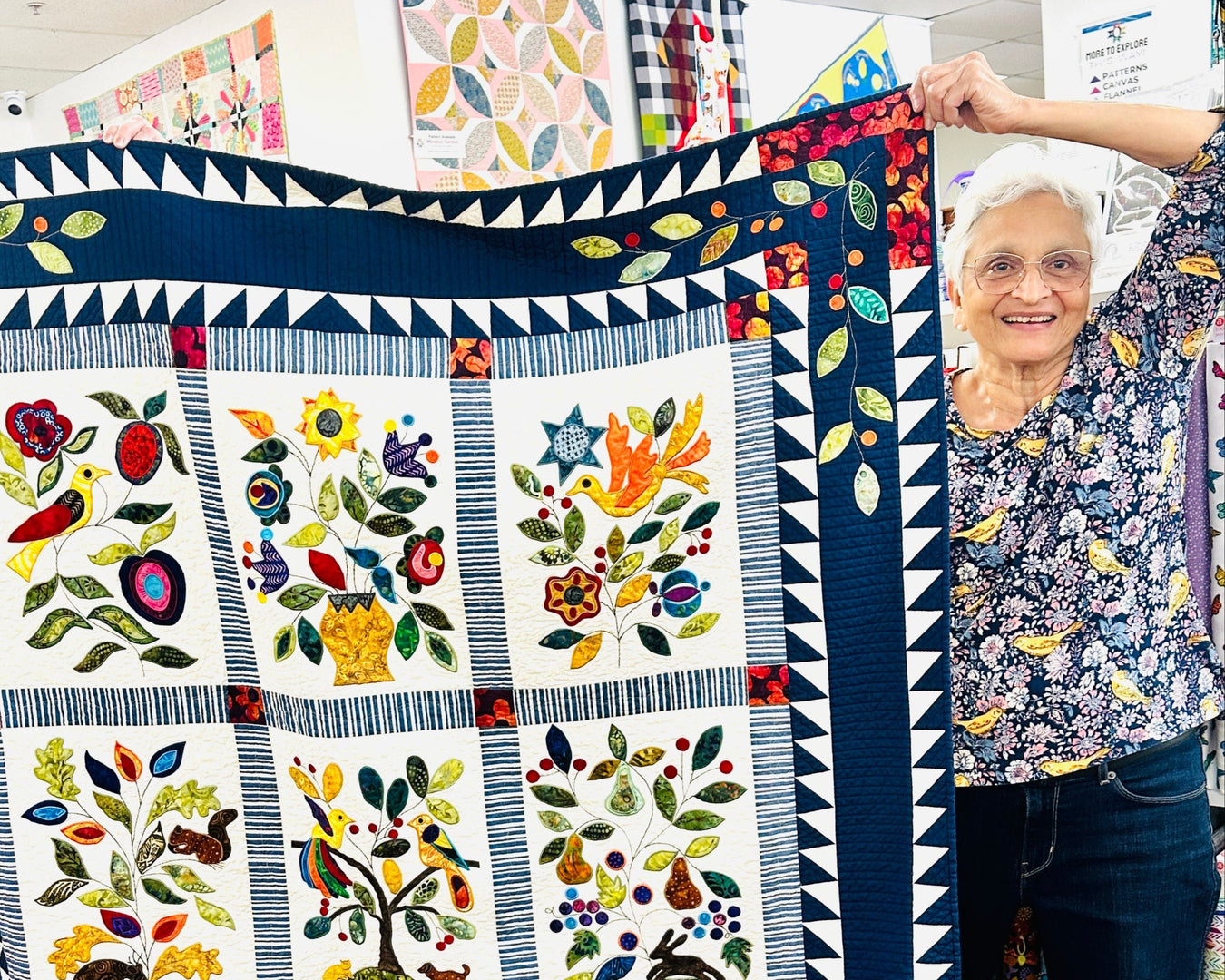 Woman holding a colorful quilt with floral and nature-themed patterns.