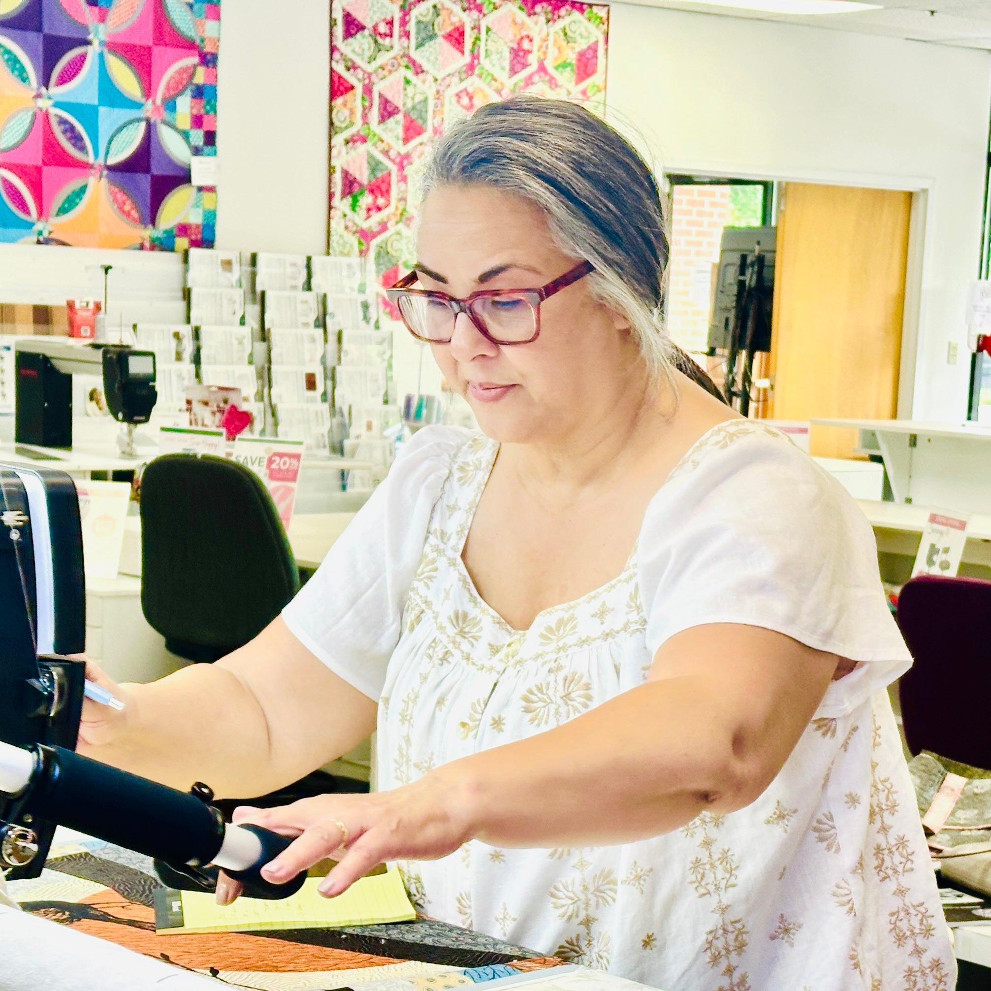 Two women working on a sewing machine in a store setting.