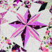 A close-up of a quilted fabric featuring a starburst patchwork design in shades of pink, purple, and white, surrounded by floral patterns.
