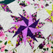 A close-up of a quilted fabric featuring a geometric star pattern in purple and pink, surrounded by white quilted sections and floral prints with green leaves and pink flowers.