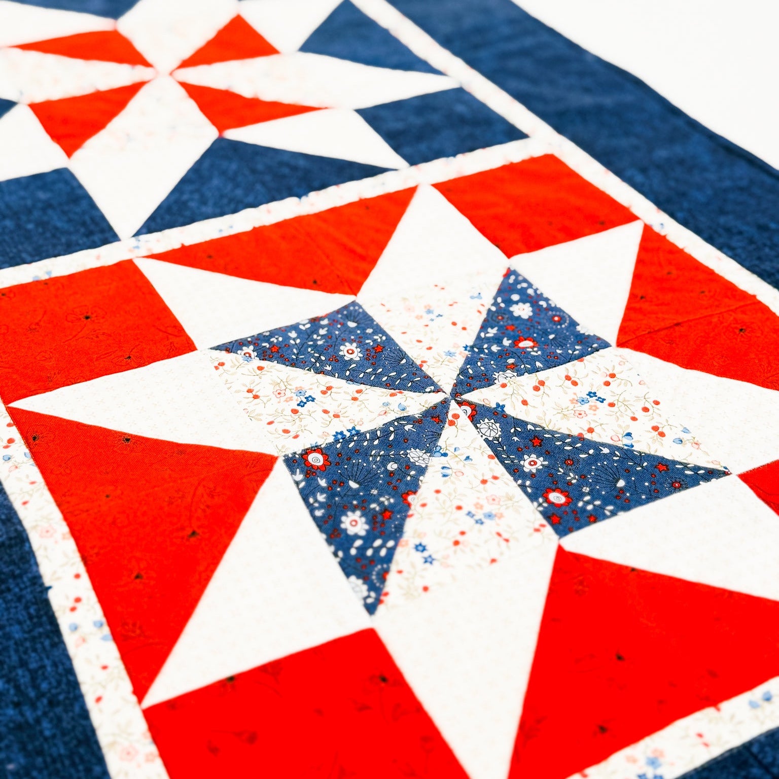 A close-up of a quilted textile with a geometric star pattern in red, white, and navy blue, including one central star with a small red, white, and blue speckled center.