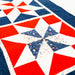 A close-up of a quilted textile with a geometric star pattern in red, white, and navy blue, including one central star with a small red, white, and blue speckled center.