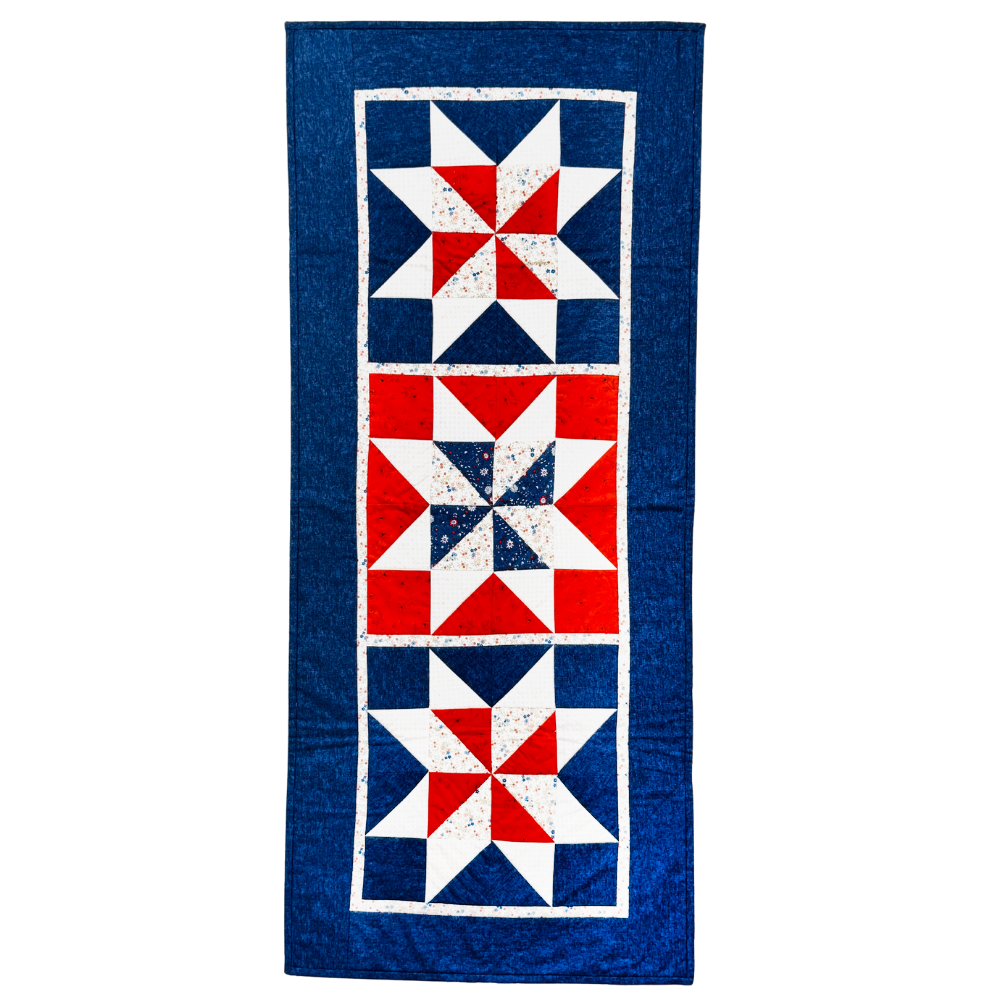 A vintage-style quilt runner featuring three vertical panels with red, white, and blue starburst patterns, finished with a wide blue border.