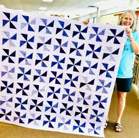 Person holding a large blue and white geometric quilt in an indoor setting.