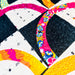 Close-up of a colorful quilted fabric with geometric and circular patchwork designs in black, white, pink, yellow, orange, and blue.