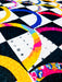 A close-up of a colorful quilted fabric with geometric and rainbow patterned sections in black, white, yellow, blue, pink, and orange.