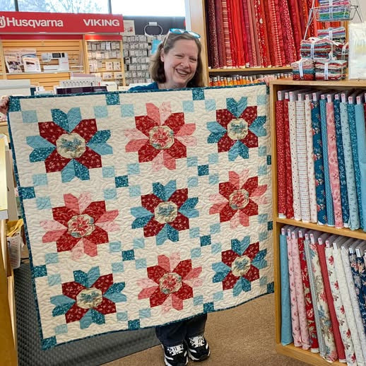 Person holding a floral quilt in front of a fabric store display