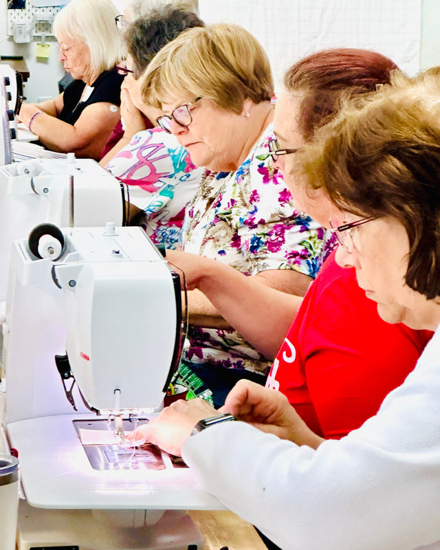 Group of people using sewing machines in a workshop setting.