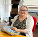 Woman sitting at a table with a decorative tray, smiling in an indoor setting.