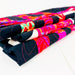 A folded quilted textile with a bold multicolor pattern, featuring black sections and bright pink, red, orange, green, and white abstract designs, photographed on a clean white surface.