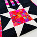 A close-up of a colorful quilted fabric featuring a star pattern with black sections, white points, and a vibrant multicolor patchwork center.
