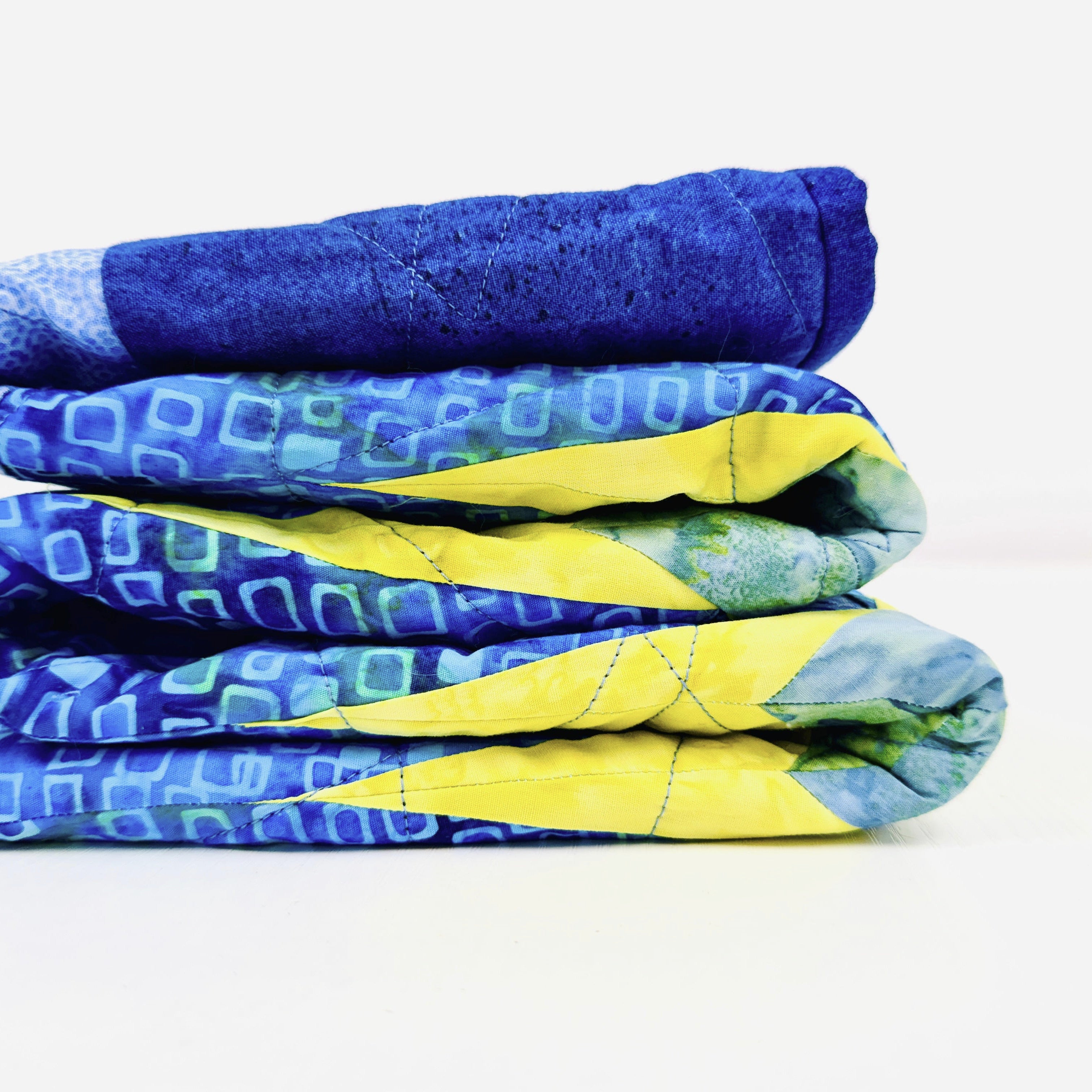 A stack of three folded quilted blankets in blue and yellow patterns, shown on a clean white background.