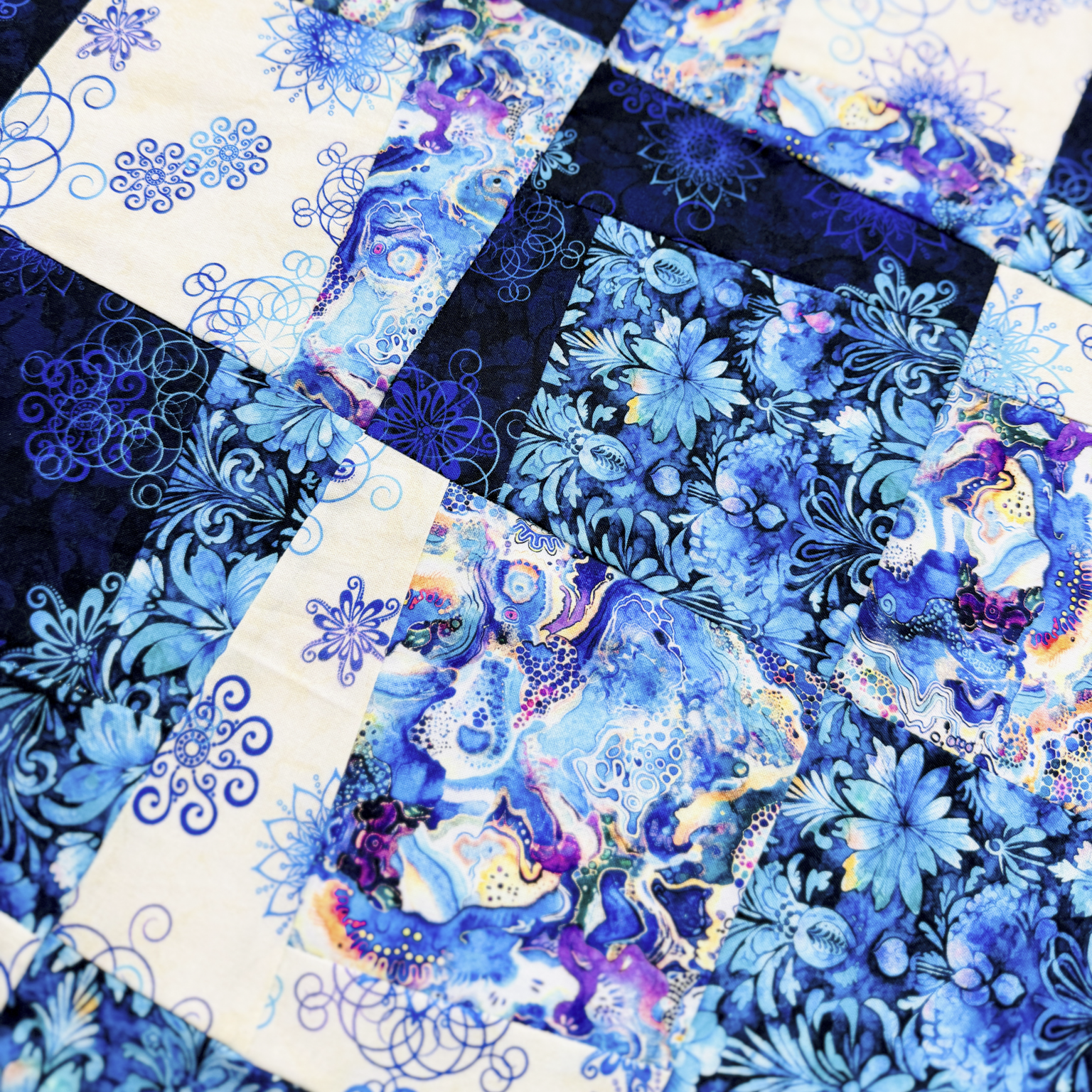 A close-up of a patchwork quilt featuring various blue and white fabrics with floral, marbled, and scroll patterns.