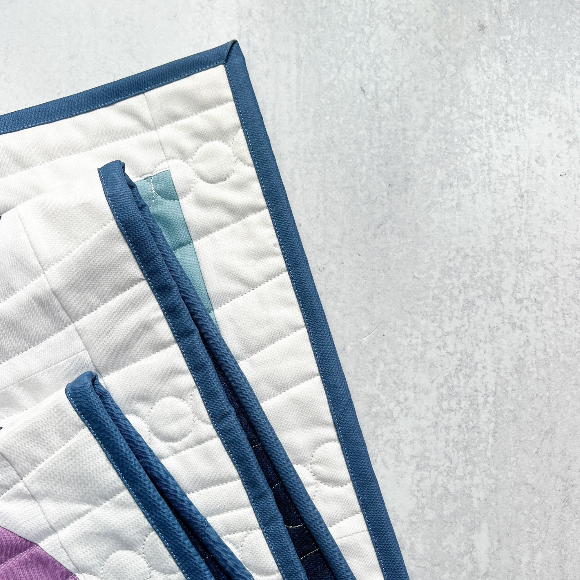 Blue fabric strips on a white quilt with purple corner