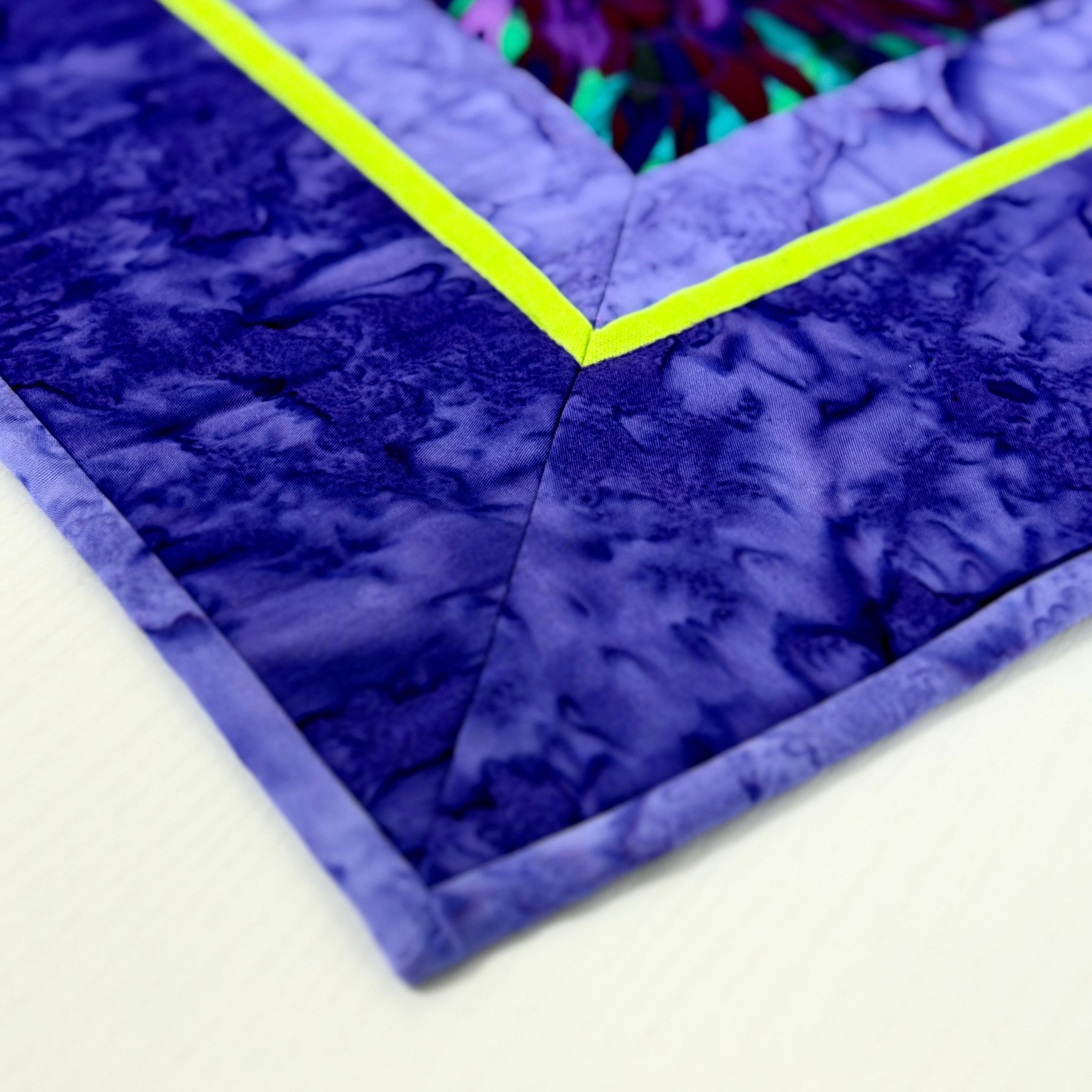 Close-up of a purple quilt with a green border on a white background