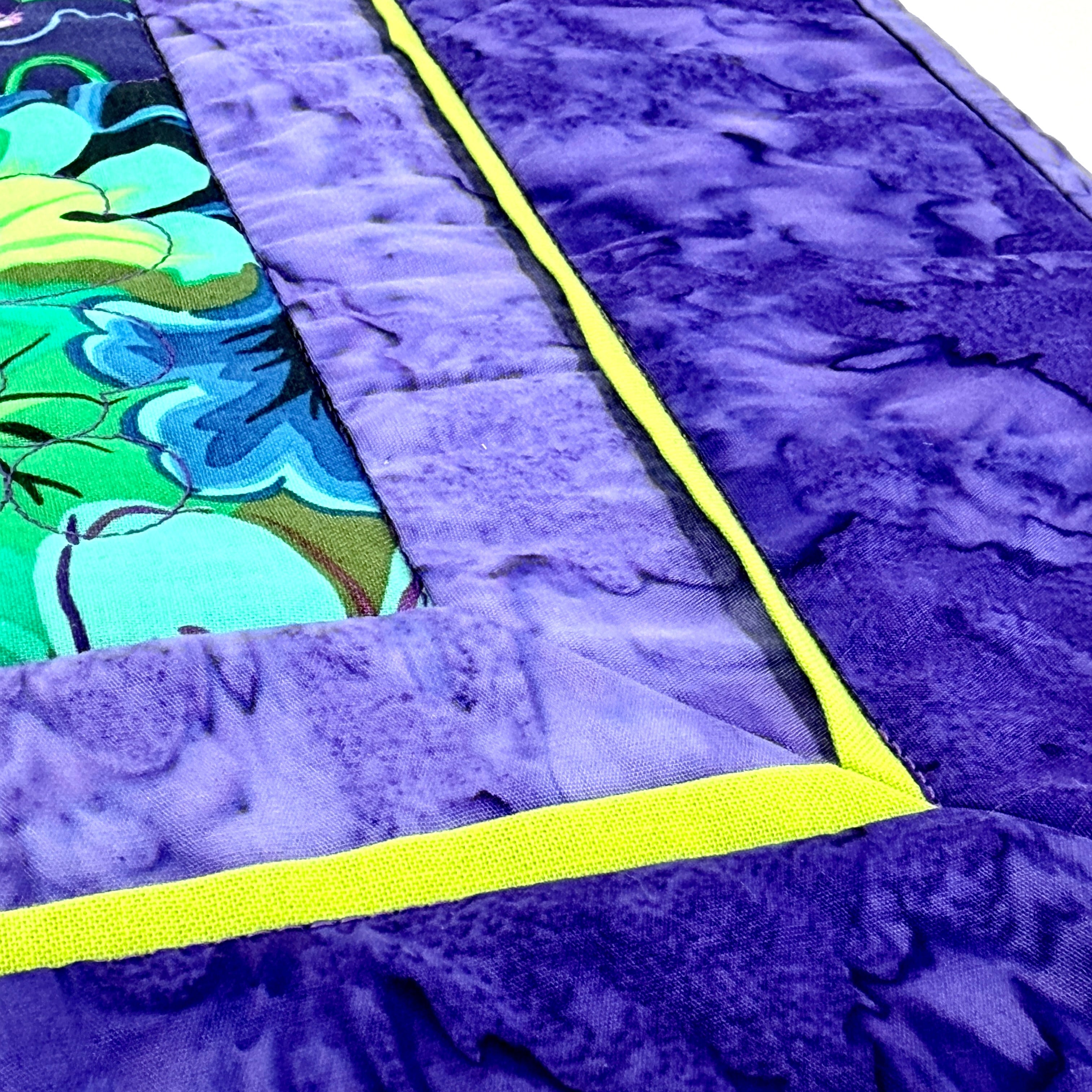 Close-up of a purple quilt with a colorful floral pattern on a white background