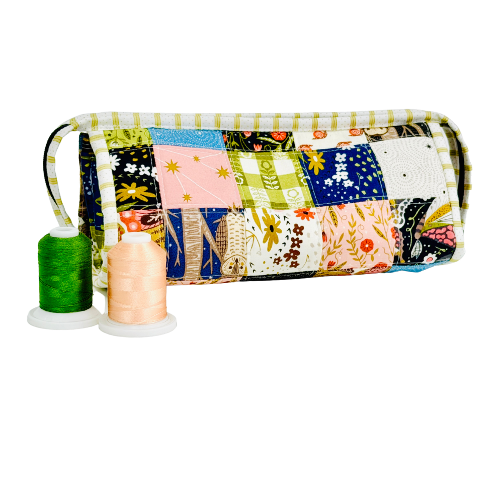 Patchwork-patterned fabric roll with spools of thread on a white background